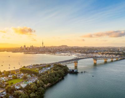 A scenic view of a city skyline at sunset, with a long bridge spanning a calm body of water. The sky is vibrant with golden hues, evoking tranquility.