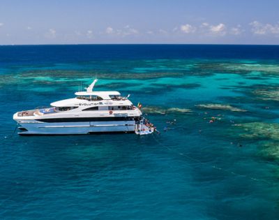 A luxury yacht anchored in clear turquoise waters near a vibrant coral reef, with snorkelers exploring the marine life. The scene is calm and sunny.