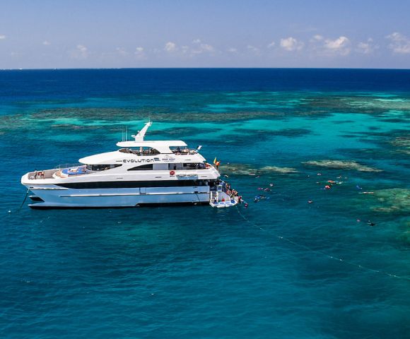 A luxury yacht anchored in clear turquoise waters near a vibrant coral reef, with snorkelers exploring the marine life. The scene is calm and sunny.