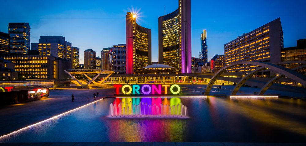 Toronto's skyline at night, featuring the illuminated city hall and a vibrant, multicolored 
