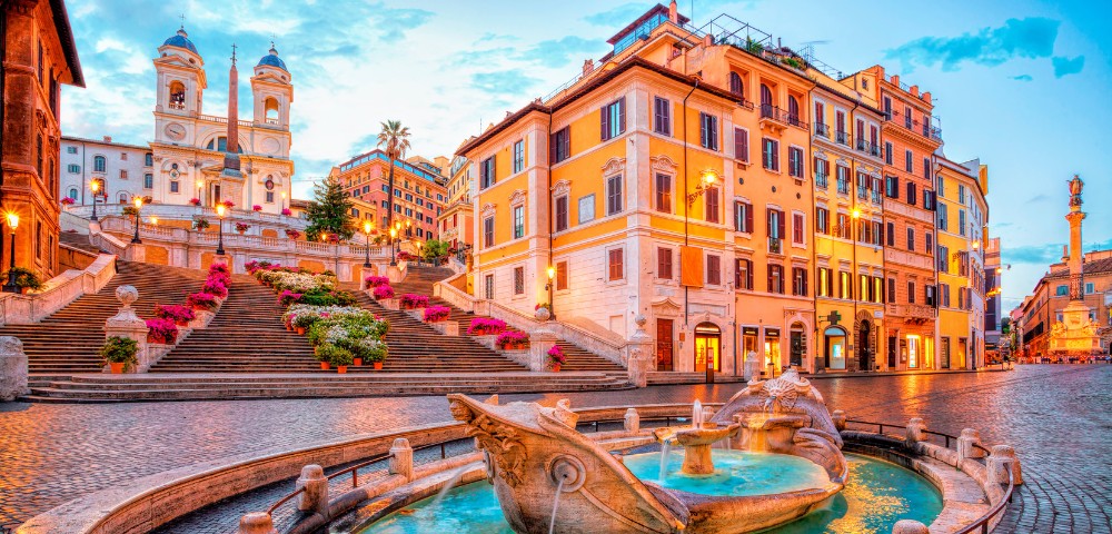 View of the Spanish Steps and Trinità dei Monti church with the Fontana della Barcaccia fountain in Rome at dusk.