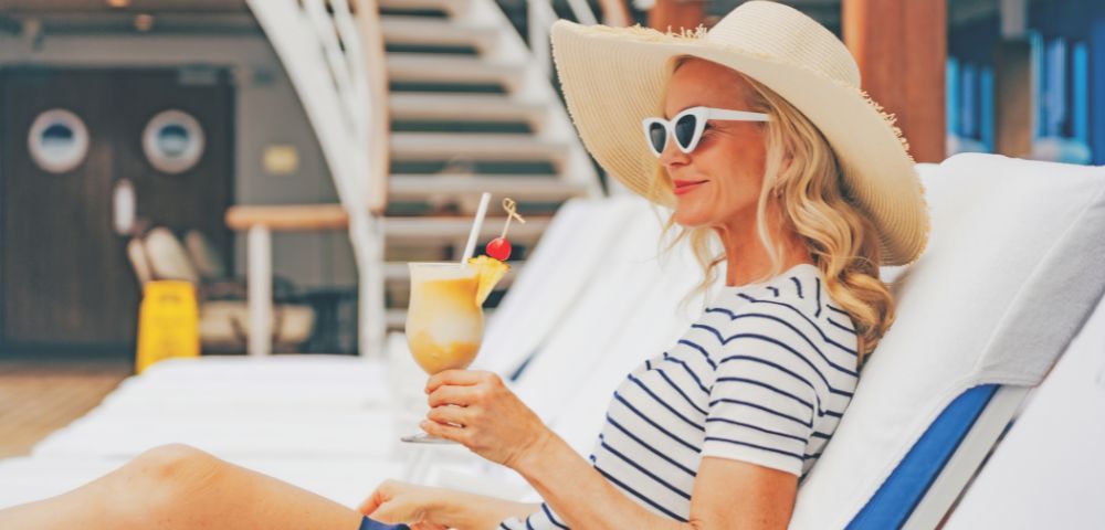 A woman wearing a striped hat and sunglasses relaxes on a lounge chair.