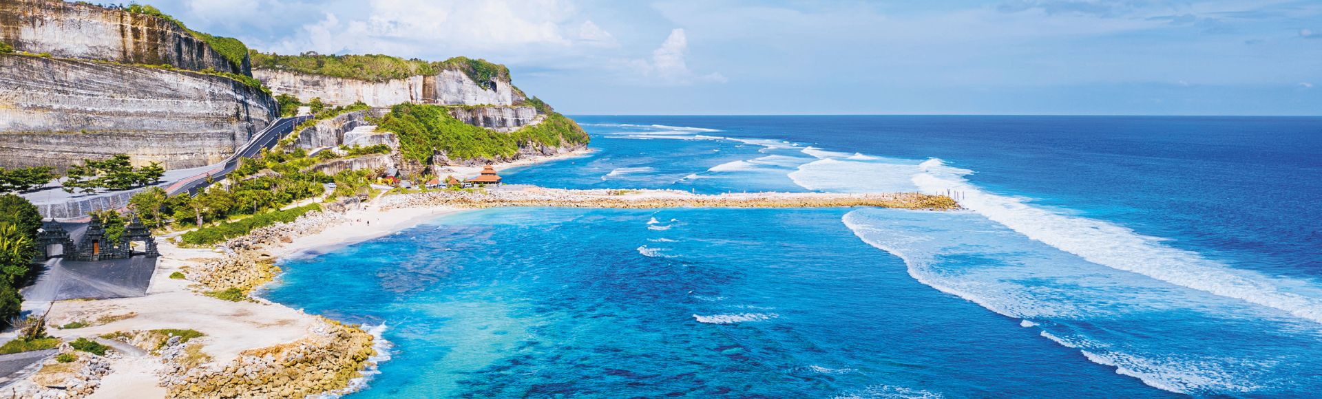 Aerial view of a stunning beach with turquoise water, gentle waves, and rocky cliffs under a clear blue sky, conveying serenity and natural beauty.