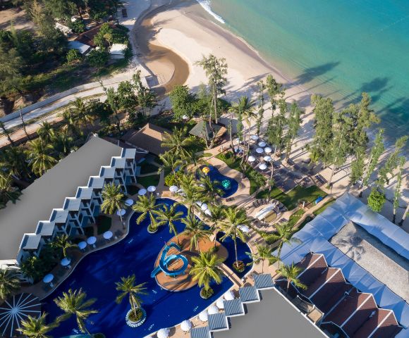 Aerial view of a tropical beach resort with turquoise sea, sandy beach, palm trees, and a curvy pool surrounded by sun loungers and villas. Peaceful ambiance.