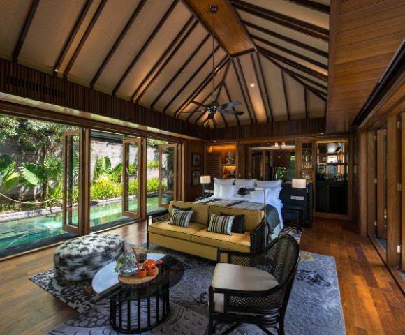Luxurious tropical bedroom with wood accents, high ceilings, and large windows overlooking lush greenery. Cozy seating, elegant decor, serene ambiance.