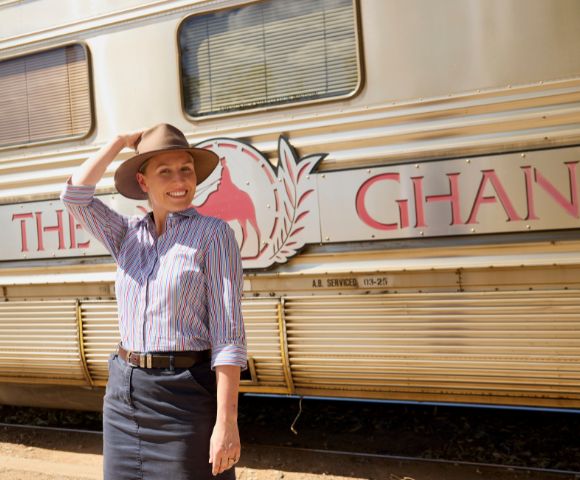 A smiling person in a hat stands in front of a train with 
