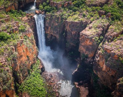 Aerial view of a waterfall cascading into a rocky gorge surrounded by lush green vegetation, conveying a sense of natural beauty and tranquility.