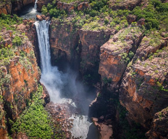 Aerial view of a waterfall cascading into a rocky gorge surrounded by lush green vegetation, conveying a sense of natural beauty and tranquility.