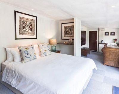 Bright, elegant bedroom with a large bed adorned with patterned pillows. Two framed artworks hang on white walls. Warm lighting from bedside lamps adds coziness.