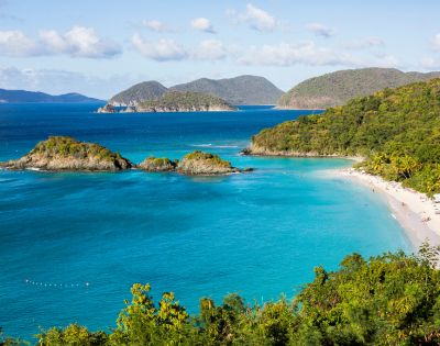 Turquoise waters surround small islands and a lush, green coastline in a tropical bay. A sandy beach curves along the shore, creating a serene and inviting scene.