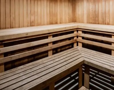 A wooden sauna interior with bench seating along two walls, featuring smooth, vertical paneling. The space appears warm and inviting, conveying relaxation.