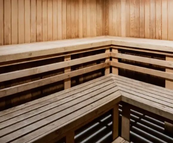 A wooden sauna interior with bench seating along two walls, featuring smooth, vertical paneling. The space appears warm and inviting, conveying relaxation.