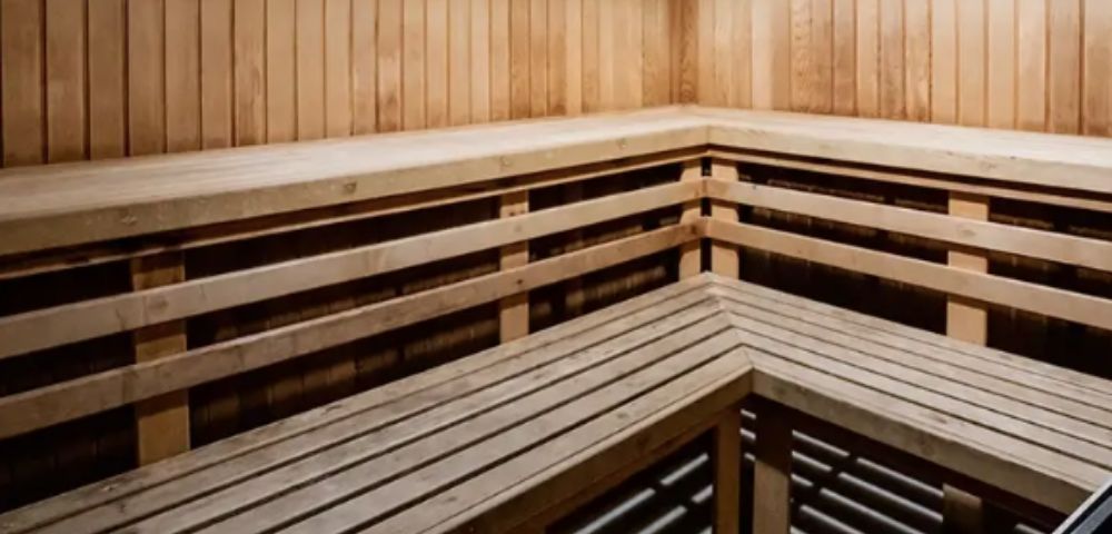 A wooden sauna interior with bench seating along two walls, featuring smooth, vertical paneling. The space appears warm and inviting, conveying relaxation.