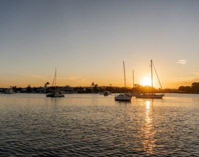 Peaceful sunset over a harbor with silhouetted sailboats on calm water, casting reflections and creating a serene, golden-hued scene.