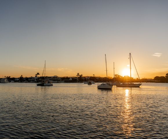 Peaceful sunset over a harbor with silhouetted sailboats on calm water, casting reflections and creating a serene, golden-hued scene.
