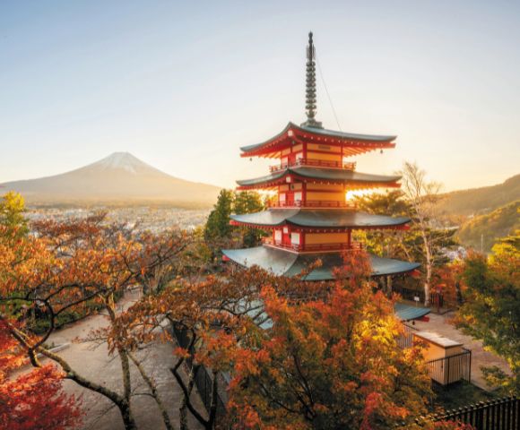 A serene landscape featuring a red pagoda surrounded by vibrant autumn trees. Mount Fuji is visible in the background under a clear, golden sky.