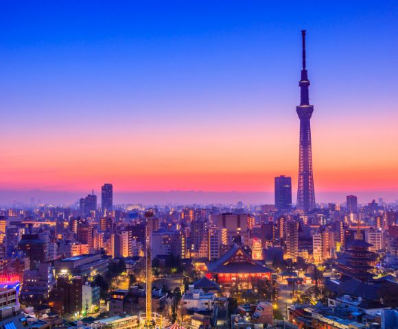 Tokyo skyline at sunset with vibrant orange and blue sky. The Tokyo Skytree stands prominently among city buildings, creating a serene urban scene.