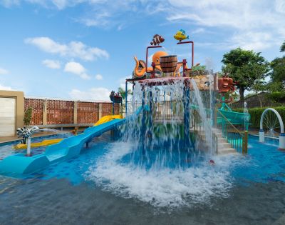 Children's water park with vibrant slides and cascading water. An octopus sculpture sits atop. The scene is playful, under a bright blue sky.