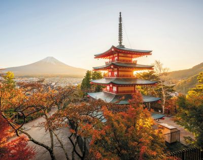 A serene sunrise illuminates a red pagoda surrounded by autumn trees, with Mount Fuji in the background under a clear sky, evoking tranquility.