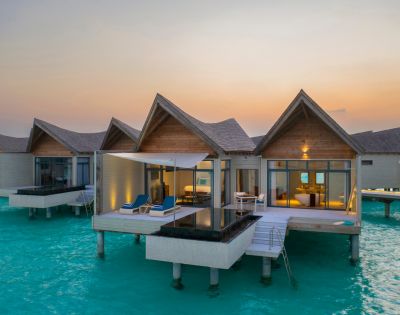 Overwater bungalows on a serene turquoise sea at sunset. Each has a private deck, plunge pool, and lounge chairs, creating a tranquil, luxurious vibe.