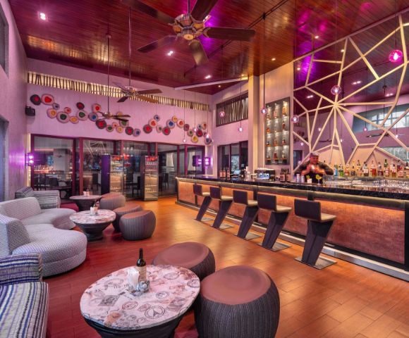Modern bar interior with warm lighting, sleek black stools along a stylish counter. Cozy seating, artistic wall decor, and a relaxed, inviting atmosphere.