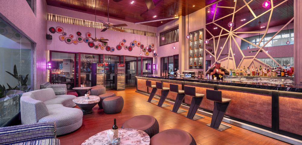 Modern bar interior with warm lighting, sleek black stools along a stylish counter. Cozy seating, artistic wall decor, and a relaxed, inviting atmosphere.