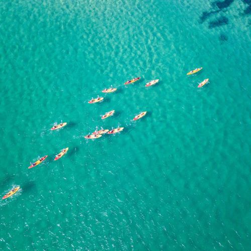 Aerial view of vibrant kayaks scattered across clear turquoise water, creating dynamic patterns. The scene conveys a sense of adventure and tranquility.