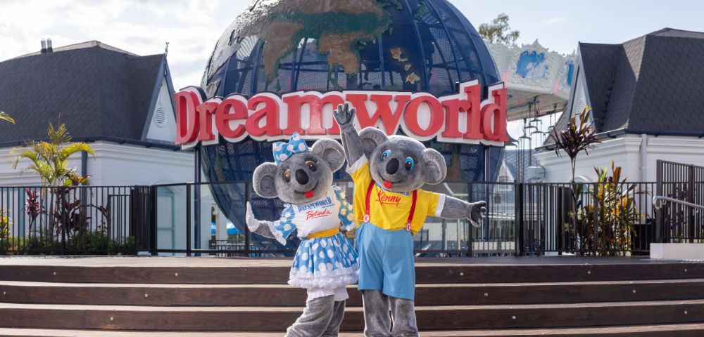 Two koala mascots in colorful outfits pose happily in front of a globe and 