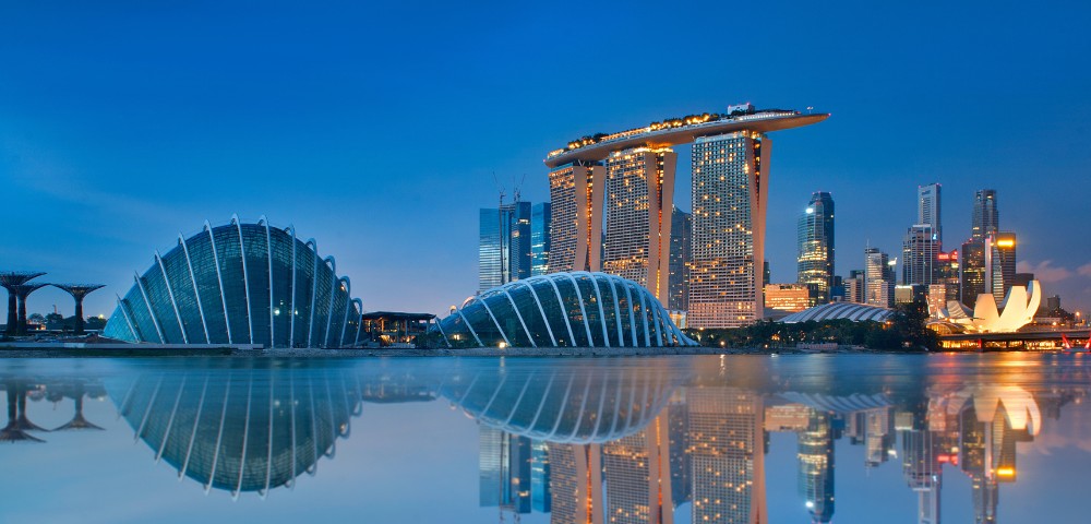 Skyline of Singapore at dusk, featuring the Marina Bay Sands hotel with its ship-like rooftop, futuristic glass domes, and city lights reflecting on calm water.