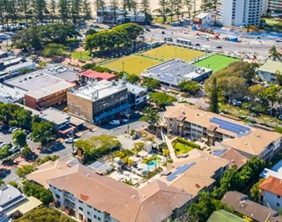 Aerial view of a suburban area with buildings and parking lots surrounded by trees. A vibrant sports field is visible, providing a lively, active atmosphere.