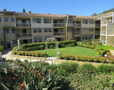 A three-story apartment building surrounds a neatly manicured central garden with lush greenery and a decorative archway, conveying a serene atmosphere.