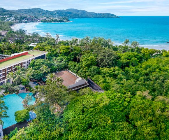 Aerial view of a resort surrounded by lush green trees near a turquoise beach. Features a large pool, palm trees, and a coastal landscape. Serene ambiance.