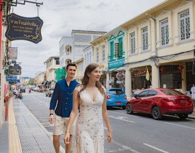 A couple strolls down a vibrant street lined with colorful, historic buildings and signs. The scene conveys a lively, cheerful atmosphere.