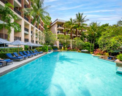 Luxurious hotel pool surrounded by lush tropical plants and palm trees, with blue lounge chairs and striped umbrellas along the deck, exuding a relaxing vibe.