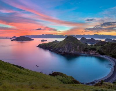 Scenic view of a tranquil bay at sunset, with vibrant pink and blue skies. Hills surround the calm water, creating a serene and peaceful atmosphere.
