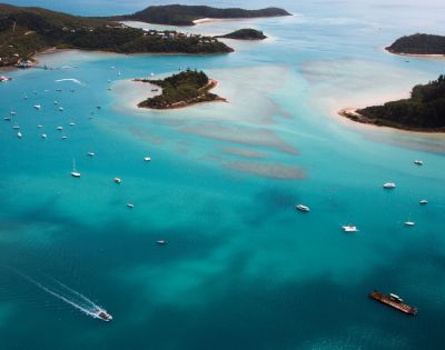 Aerial view of turquoise ocean with numerous boats near small, green islands and sandy beaches, evoking a serene and tropical atmosphere.