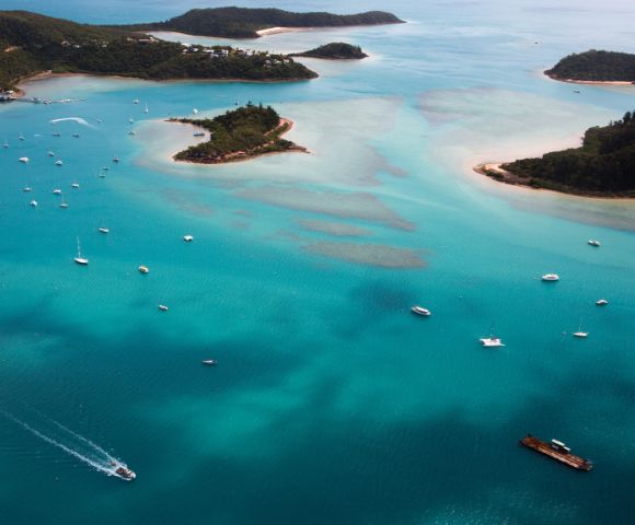 Aerial view of turquoise ocean with numerous boats near small, green islands and sandy beaches, evoking a serene and tropical atmosphere.