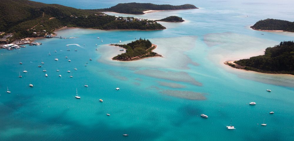 Aerial view of turquoise ocean with numerous boats near small, green islands and sandy beaches, evoking a serene and tropical atmosphere.