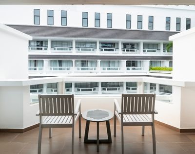 Balcony view with two wooden chairs and a small round table overlooking a modern white building with multiple windows and balconies.