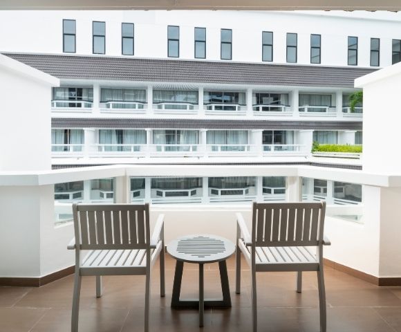 Balcony view with two wooden chairs and a small round table overlooking a modern white building with multiple windows and balconies.