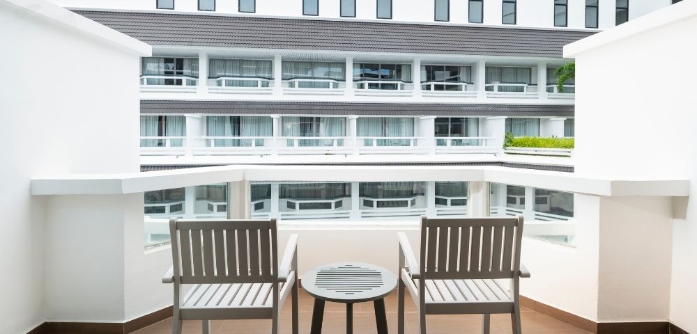 Balcony view with two wooden chairs and a small round table overlooking a modern white building with multiple windows and balconies.