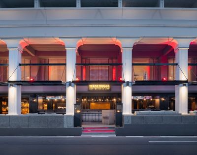 Facade of a stylish bar with columns and red lighting. The entrance features a warm glow and the text 