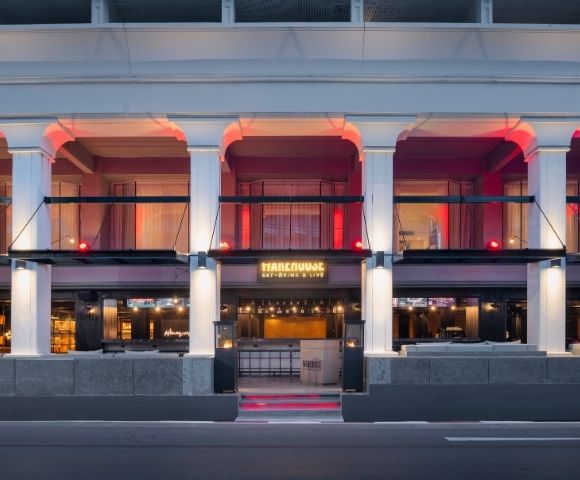 Facade of a stylish bar with columns and red lighting. The entrance features a warm glow and the text 