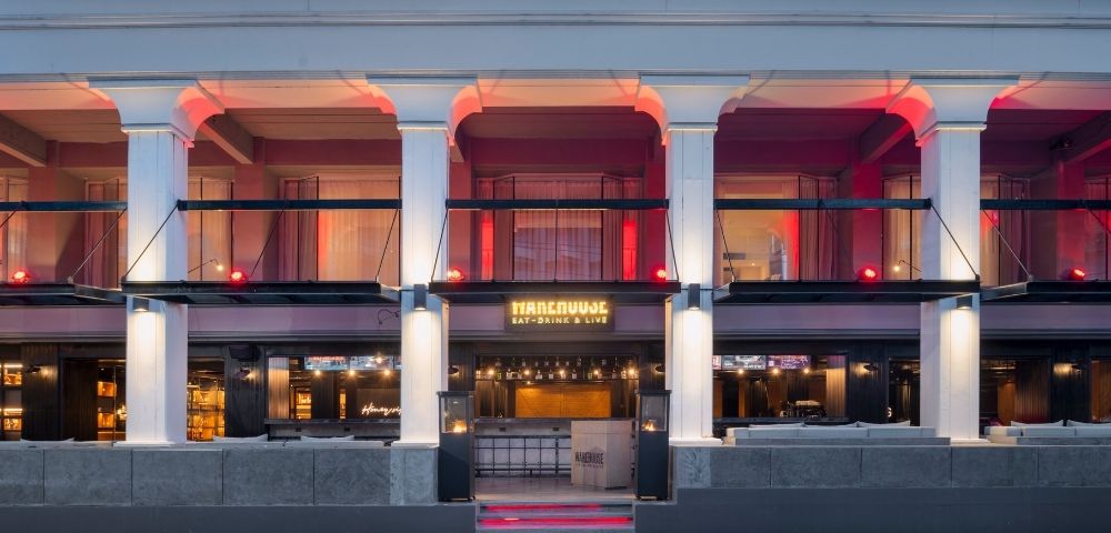 Facade of a stylish bar with columns and red lighting. The entrance features a warm glow and the text 
