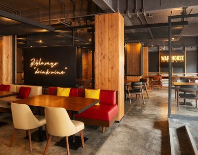 Modern cafe interior with warm lighting, wooden accents, and red cushioned seating. Neon signs read 