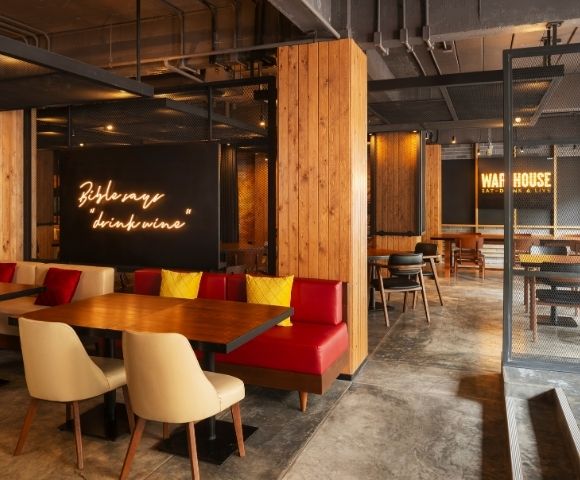 Modern cafe interior with warm lighting, wooden accents, and red cushioned seating. Neon signs read 