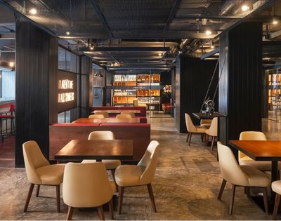 Modern restaurant interior with warm lighting, wooden tables, beige cushioned chairs, and decorative shelves. Cozy and inviting atmosphere.
