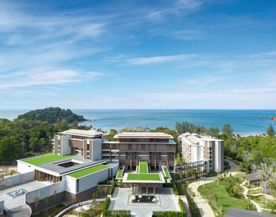 Modern beachfront resort surrounded by greenery with green rooftop terraces and ocean views under a blue sky.