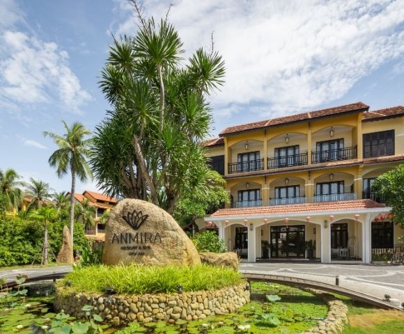 Anmira Resort & Spa building with a rock sign, surrounded by palm trees and greenery under a partly cloudy blue sky.