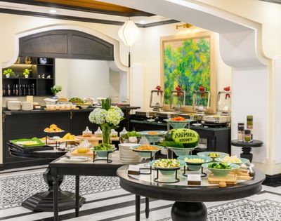 Buffet setup in a stylish dining area with tables of salads, dishes, bread, and a colorful painting on the wall.